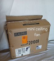 Photo of the front side of the cardboard box for the Flalinko mini ceiling fan with brand name, model number F201009, and handling instructions visible.