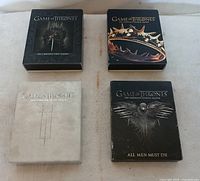 Four DVD sets of Game of Thrones Seasons 1 to 4 in original cases laid out on a soft beige surface.