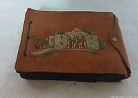 Closed view of the brown leather photo album with hand-painted San Jacinto building and landscape on the front cover.