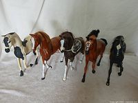 Group of five horse figurines standing on a white cloth background, showing variety in color and pose