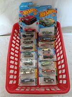 Group photo of all 16 Hot Wheels cars in original packaging arranged in a red plastic tray.