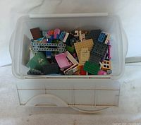 View of assorted colored Lego pieces spread inside a transparent plastic bin with lid shown beneath.