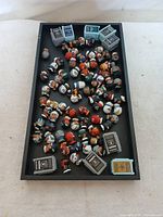 Overview of approximately 50+ NFL Teeny Mates figurines and multiple NFL helmet mini collectibles displayed loosely in a black tray on a fabric surface.