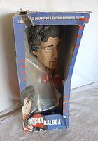 Front view of Rocky Balboa animated figure in original packaging showing visible facial features of the figure and damaged torn box.
