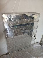 Front and side view of tall rectangular acrylic display case featuring rows of circular compartments designed to hold baseballs. Clear acrylic construction with lock and key on the right side door.