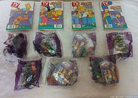 Photo of 4 Simpsons-themed TV Guide collector magazines and 7 unopened 2001 Burger King Spooky Meal Toys in original sealed purple packaging.