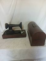 Vintage Singer sewing machine on wooden base with electric motor and separate wooden carrying case beside it.