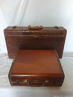Photo showing the exterior of one large textured brown suitcase and one smaller smooth brown Samsonite suitcase stacked together