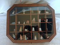 Octagonal wooden display case with glass top showing 24 individual compartments holding assorted ceramic and metal sewing thimbles.