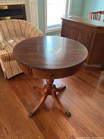 Full front view showing round top, pedestal base, curved legs with brass claw feet, and drawer front with knob.