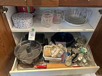Two kitchen shelves showing baking supplies including glass measuring cups, pie plates, metal pans, a rolling pin, cookie cutters, and other baking tools
