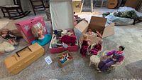 Wide view of dolls, doll clothes, furniture, and accessories arranged on carpet