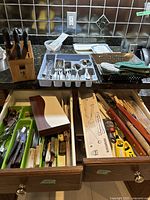 Wide shot showing kitchen drawers with cutlery tray containing forks, knives, spoons, and stainless BBQ tools including grill basket and tongs.