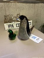 Two glass bird figurines placed on a surface, larger black and white striped one and smaller green and yellow one