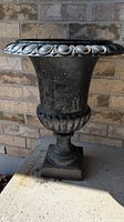 Front and side view of the black cast iron urn planter showing the shape, decorative fluted rim and weathered surface.