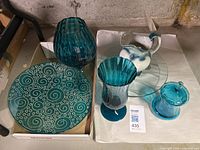 Overview of all items showing teal glass plate with glitter spirals, teal vase, teal jar with lid, ceramic jug with blue decoration, clear glass plate.