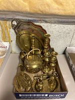 Overall assortment of brass items including trays, teapot, candle holders, and key holder arranged in a box.