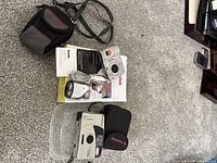 Photo showing the two cameras, FujiFilm Clear Shot and Kodak EasyShare, along with Kodak camera's accessories including USB cable, battery, carrying case, and instruction manual.
