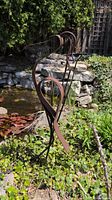 Side view of cast iron heron sculpture in garden setting showing elongated neck and body curves with patina finish