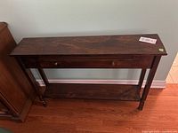 Front view of the slim console table showing the faux drawer and lower shelf with slight damage on front legs.