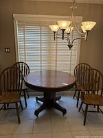 Front view of tiger oak round dining table with four matching chairs in front of window with blinds