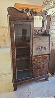 Full front view of dark brown tiger oak display cabinet with drop-front secretary and glass-front shelving