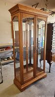 Front and side view of tall quarter sawn oak display cabinet with glass doors and shelves.