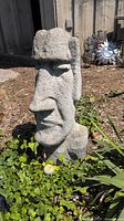 Front view of concrete Easter Island Head statue outdoors among plants.