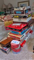 Stack of classic board games including Monopoly, Othello, Uno, Backgammon, Master Mind, Gambler, and Triple Yahtzee. Shows original game boxes with vintage graphics and colors.