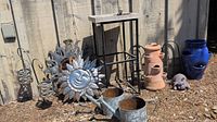 Full lot showing terracotta stacked strawberry planters, blue glazed planter, old metal watering cans, metal sun wall art, terracotta bird bath planter turtle, and crab motif candle holders on hooks.