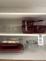 Upper shelf showing purple glass cookware, including two casserole dishes with lids and handles, and clear glass round bowl with lid.