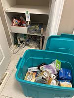 Wide view of plastic bins filled with assorted household items and shelving with chair pads and power cords.