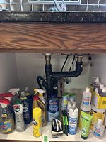 Wide view of cleaning products under kitchen sink showing many spray bottles, aerosol cans, and wipes
