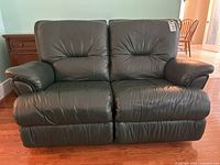 Front view of dark green leather loveseat showing two seats and padded armrests