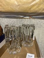 Two clear glass luster candle holders with floral bases and hanging rectangular prisms inside a cardboard box.