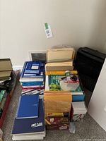Photo showing stacks of assorted reams of copy paper, envelopes, file folders, and notebooks arranged on carpeted floor.