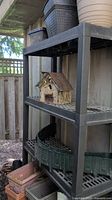 Plastic shelving unit holding various plastic planters and a wooden bird house on middle shelf viewed from a distance, showing overall lot contents and condition.