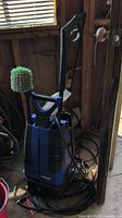 Full view of blue and black Simoniz 1700 power washer with wand and green circular brush, coiled cable on floor.