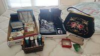 Wide angle photo showing boxes of costume jewellery, ladies watches, two black boots, needlepoint purse and leather change purse on mattress.