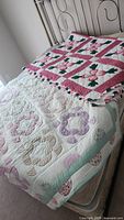 Both quilts displayed on bed showing pastel applique quilt with mint green border and bright pink and green applique quilt with handkerchief hem.