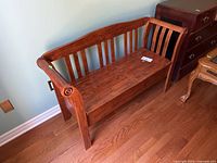 View of wooden storage bench from front showing back and armrests, medium wood tone finish, surface scratches visible.