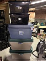 5 stacked storage totes including 2 Rubbermaid RoughTote, 1 Gracious Living ProTote, and 2 KIS totes in basement setting.