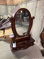 Front view of dark wood oval table mirror with decorative scroll details and 3 drawers at base, showing overall condition.