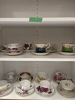Full view of 14 teacups and saucers arranged on shelves showing various floral and color patterns