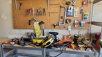 Overall view of workbench and pegboard with various small hand tools, power drills, extension cords, and hardware items.
