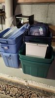 Stacked blue Rubbermaid Roughneck storage totes, some with tags and snap-on blue lids, showing different sizes.