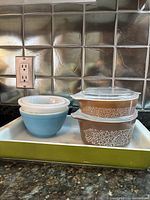 Green Pyrex rectangular baking dish, brown Woodland lidded casseroles, blue bowl visible in the background.
