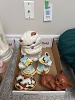 Photo of the full lot with all ceramic figurines including large white cat, dog bookends, brown cat, and Siamese mother with kittens in basket