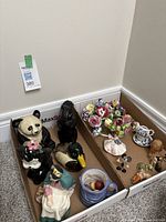 Overview of multiple ceramic and porcelain figurines including panda, squirrel, duck, skunk, lady with balloons, and floral arrangements.