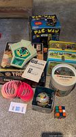 Lot spread on carpet showing all items: Coleco baseball game, Pac-Man box, Trouble game box, slinky, Rubik's cube, View-Master container, Disney lunch pails.